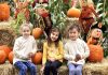 three kids sitting on a hay bale in front of pumpkins and corn stalks at the Camas Farmer's Market Harvest Festival