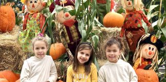 three kids sitting on a hay bale in front of pumpkins and corn stalks at the Camas Farmer's Market Harvest Festival