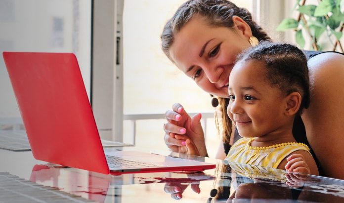 a woman and a child sitting at a table looking at a red laptop