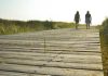 two people walking on a boardwalk at the beach
