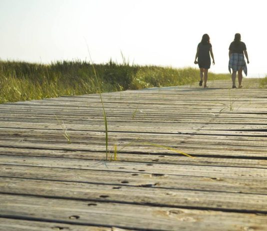 two people walking on a boardwalk at the beach